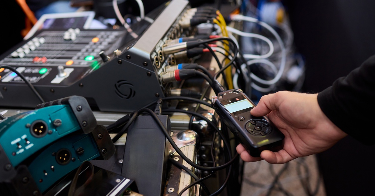 A close-up of a hand holding an audio measuring tool next to a wireless audio system for event production.